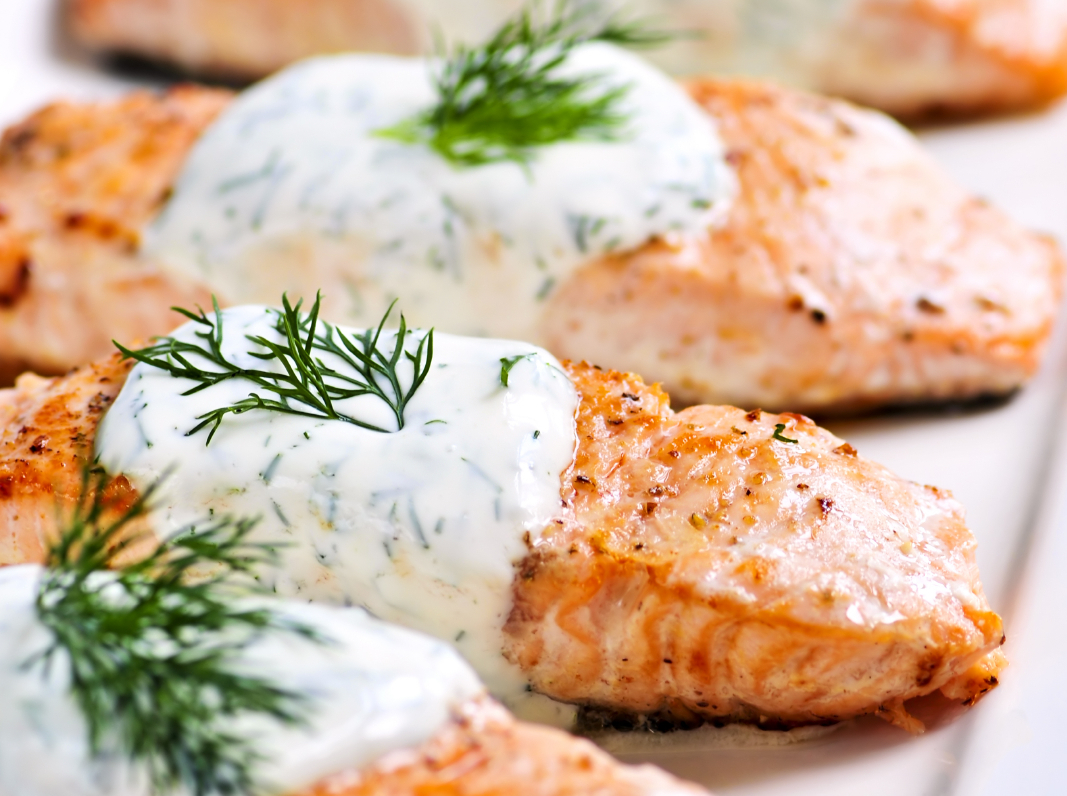 Cooked salmon fillets with dill sauce on white plate